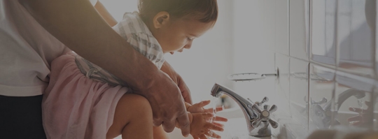 A parent helping their young child wash their hands
