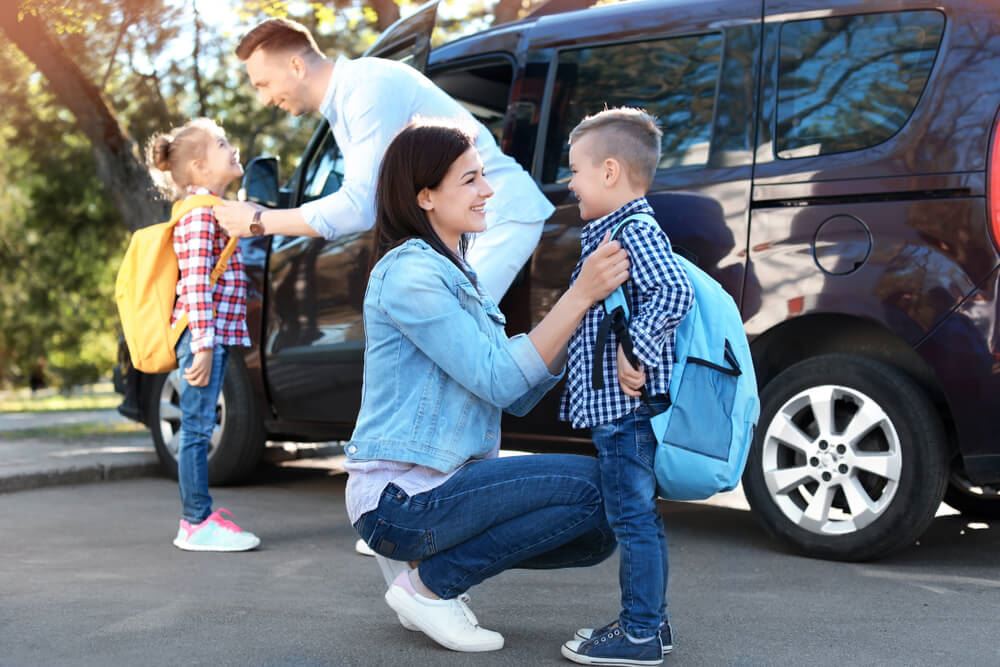 Parents putting backpacks on their children while standing by a van
