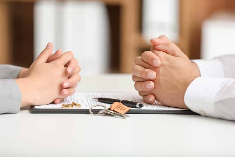 couple with hands crossed over a contract with wedding rings and house keys on the contract